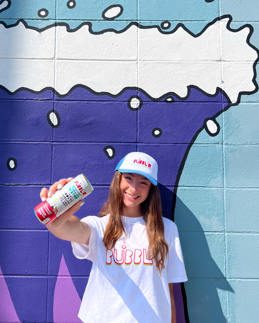 Young woman wearing soft bubbl'r trucker cap in front of painted brick wall